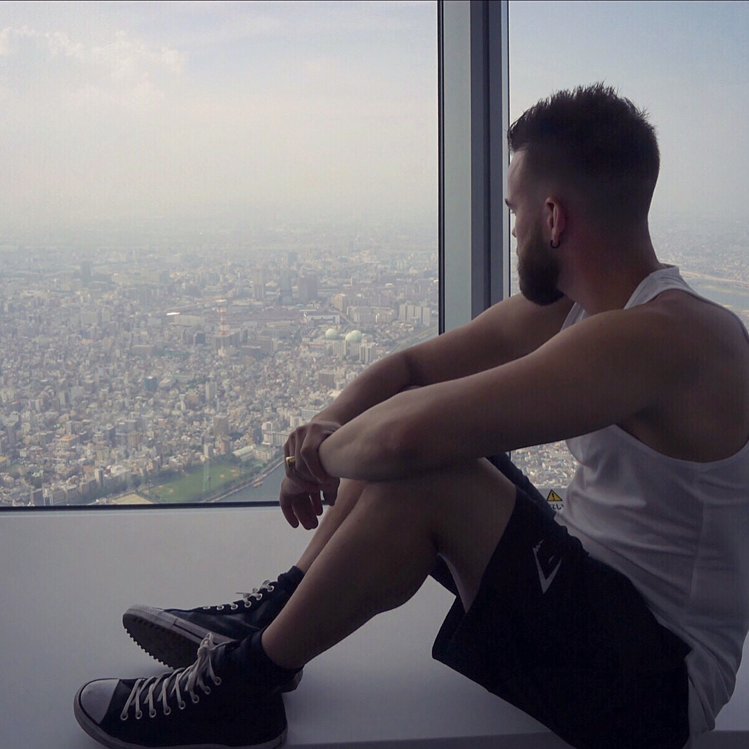 Arnaud Bruckler assis contre la baie vitrée d'une tour, Tokyo étendue en contrebas